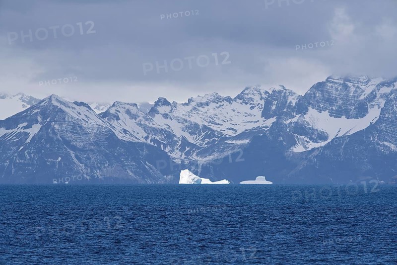 Icebergs floating in front of snow-covered coastal mountain chain, cloudy sky, South Georgia, South Atlantic
