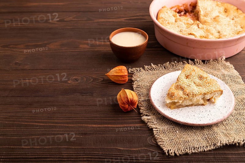 Apple Charlotte cake on brown wooden background and linen textile, cup of milk, side view, copy space
