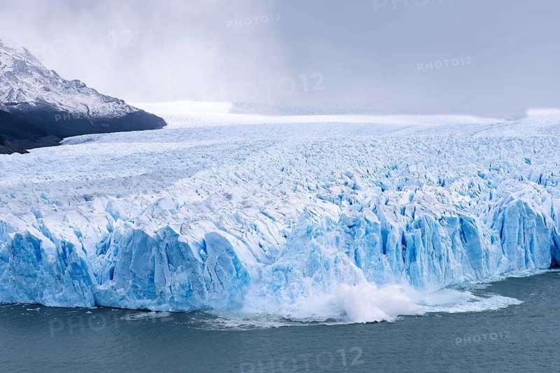 Perito Moreno glacier, breakaway with calving ice on Lake Argentino, blue glacial ice with crevices, snow-covered mountains in clouds behind it, Los Glaciares National Park, Santa Cruz Province, Argentina