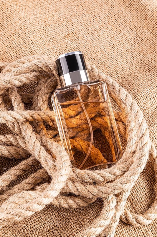 A sophisticated male perfume bottle nestled in a rustic rope set against a burlap background, showcasing an elegant blend of style and texture for a classy yet rugged aesthetic