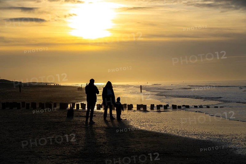 Winter on the North Sea, sunset at sea, beach walkers, coastal protection, through wooden posts, paalhoofden, on the beach, breakwater, the piles rammed into the sandy soil in double rows slow down the waves and ocean currents and thus slow down the flow rate of seawater, so less sand is washed away from the standing position, near Domburg, Walcheren peninsula in the Dutch province of Zeeland