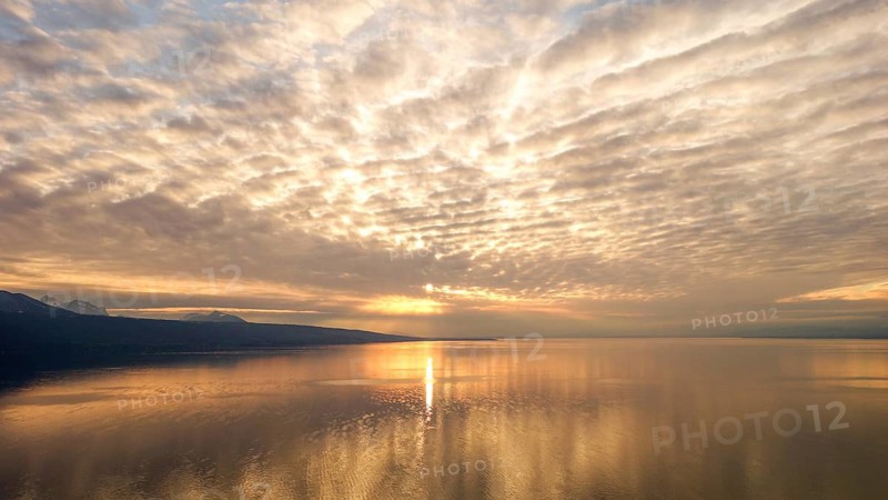 A breathtaking view of a serene sunset on Lake Geneva, with the Swiss Alps in the background. The golden sky artistically blends with peaceful waters, creating a picturesque scene