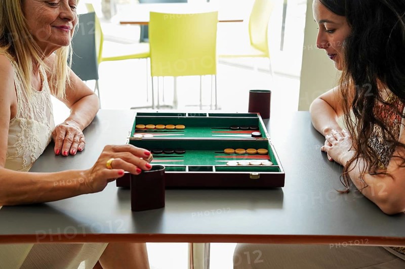 Mother and daughter enjoy a leisurely backgammon game at a modern cafe The board, with its classic design, is set on a sleek table, capturing a moment of strategy and relaxation