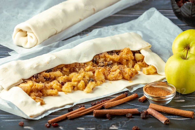 Dough with apple filling for a strudel is rolled up