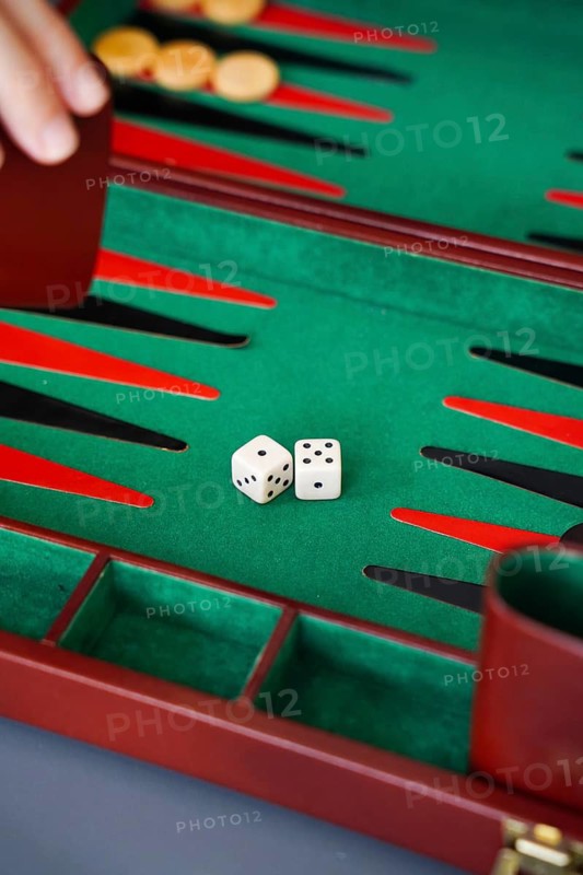 Close-up of a backgammon game with dice on a green board A hand holds the doubling cube, enhancing the game's strategic aspect Ideal for board game enthusiasts