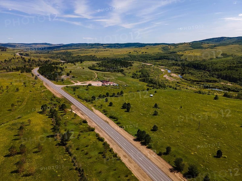 A vast expanse of green fields stretches across the landscape in Vladivostok, Russia. Winding roads lead through the natural scenery, showcasing the beauty of the area. Gentle hills frame this peaceful and tranquil environment