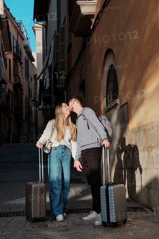 A young couple with luggage strolls through the charming, sunlit streets of Majorca, Spain, possibly searching for their dream vacation home. Romantic and adventurous vibes