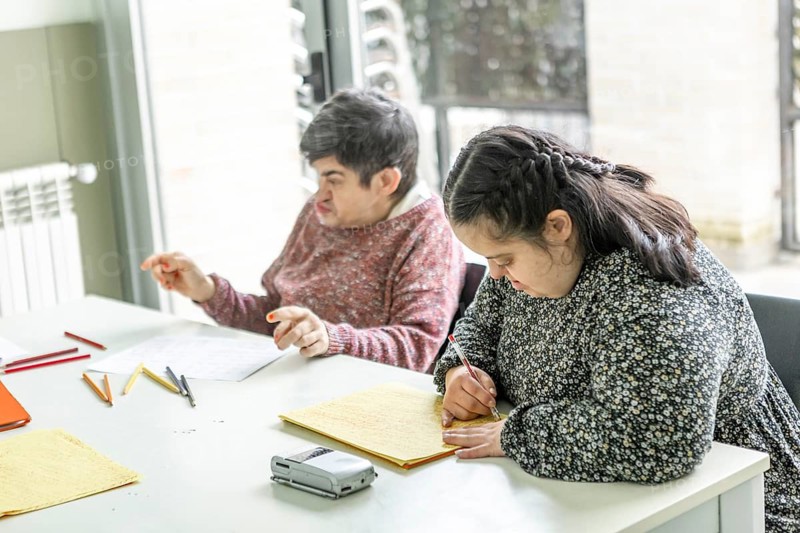 Two individuals at a mental health residence engage in creative activities. One is writing and the other drawing, fostering a supportive and nurturing environment