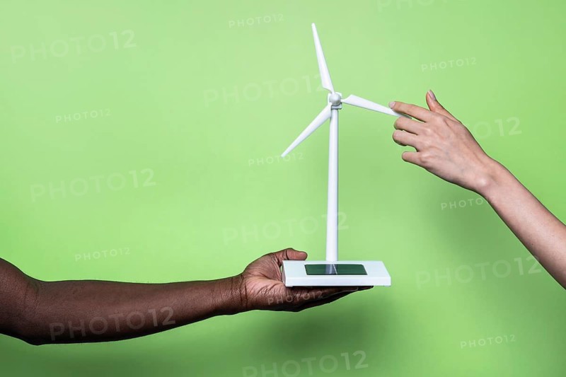 Two hands hold a miniature wind turbine, symbolizing collaboration in sustainable energy. The vibrant green background highlights eco-friendly initiatives and renewable energy solutions