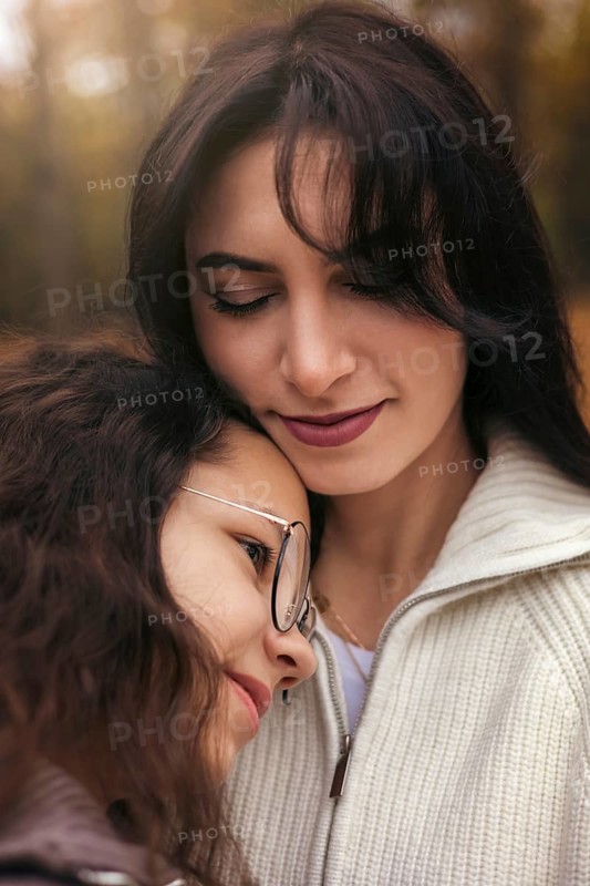 A tender moment between a mother and daughter in an autumn forest setting. They share a loving embrace surrounded by warm, golden leaves, symbolizing family warmth and connection