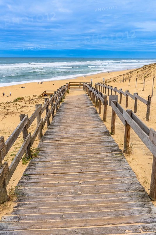 Wooden boardwalk leads down to sandy landes beach and atlantic waves under a clear blue sky, a serene coastal scene evoking summer vacation, freedom and peaceful escape