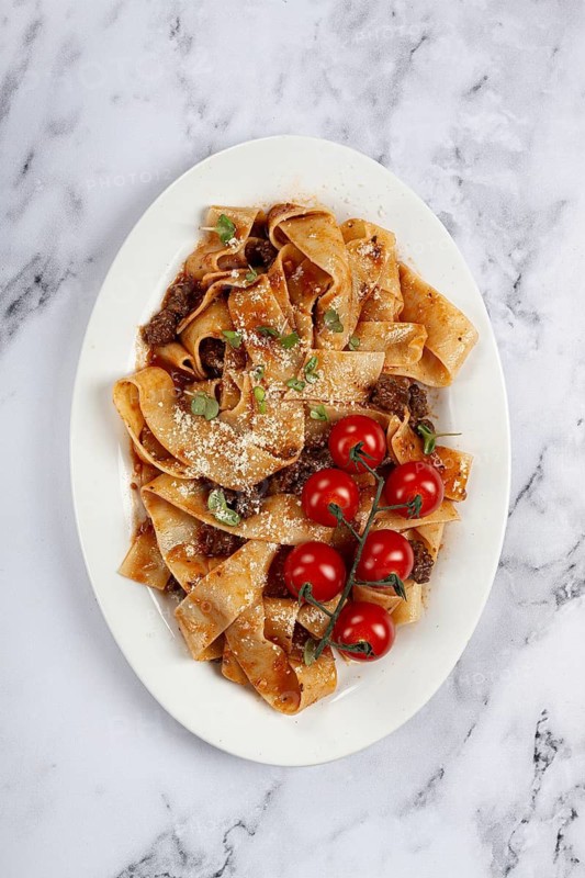 Pappardelle pasta with bolognese sauce, topped with parmesan cheese and cherry branch, homemade, no people