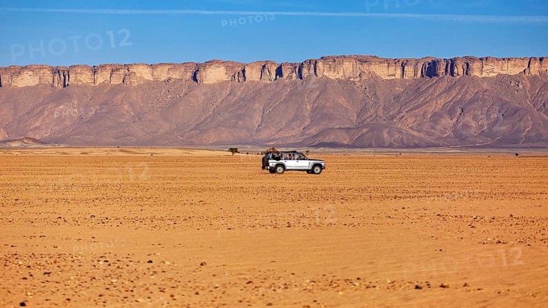 A lonely off-road vehicle in the vast, barren desert landscape with rock formations, By off-road vehicle through the endless landscape of the Sahara desert in Algeria
