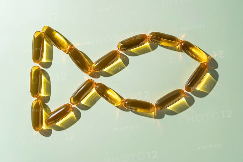 Top view of golden Omega 3 fatty acid capsules artistically arranged in a circular loop resembling a fish on a soft green background, emphasizing health and nutrition