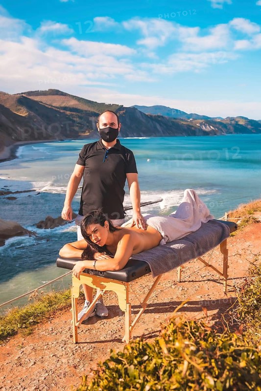 A young man performing a nature massage on the coast near the sea, a dream come true, masseur with face mask in the pandemic