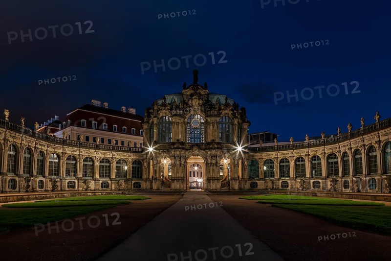 The Zwinger Palace in Dresden, Germany, is beautifully illuminated under a deep blue night sky. This baroque architecture marvel features symmetrical pathways and ornate facades