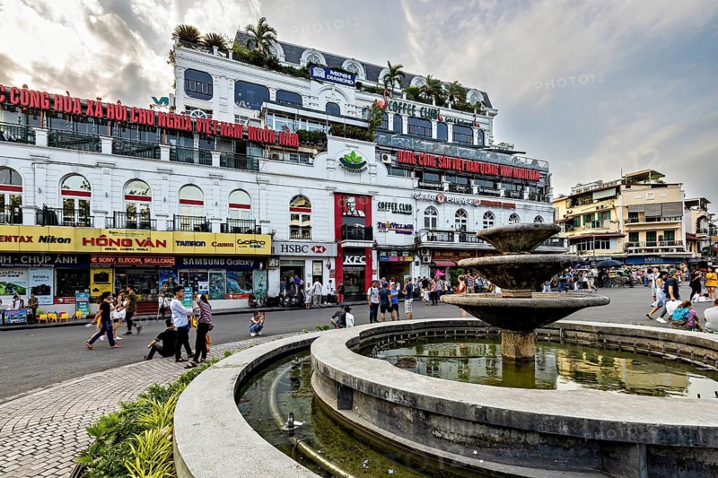 Busy urban scene with shops, people and a fountain in front of a multi-storey building, Dong Kinh Nghia Thuc Square in Hanoi, Vietnam