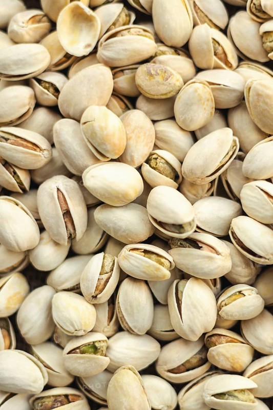 A detailed close up of pistachios in their shells, showcasing the texture and subtle colors. Perfect for use in culinary or nutrition themed designs, emphasizing natural snacks