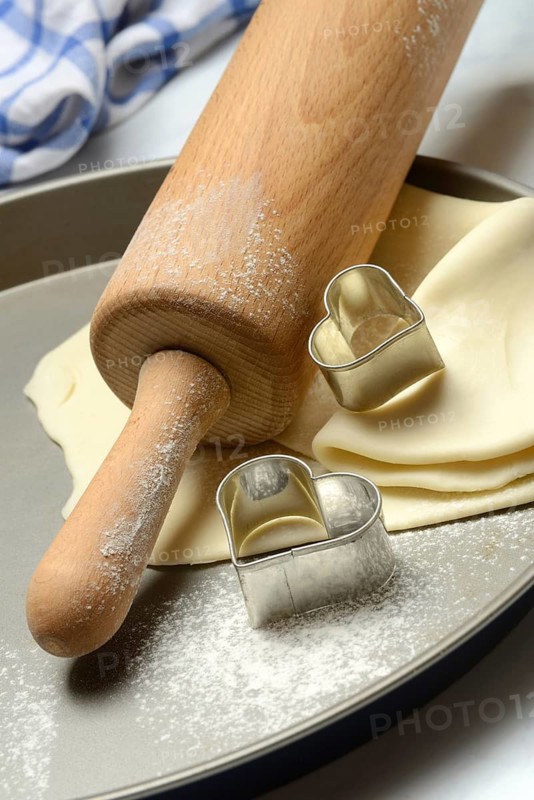 Rolled dough on cake tray with dough rollers and cookie cutters
