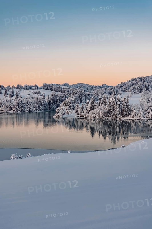Dawn and sunrise at the wintry Forggensee in a snow-covered winter landscape in the foothills of the Alps in the Allgäu in Bavaria, Germany