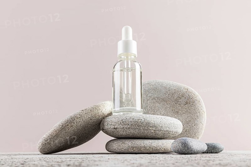 A minimalist composition featuring a dropper serum bottle balanced on smooth gray stones The serene arrangement embodies a spa-like atmosphere of relaxation and balance