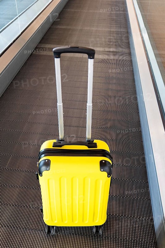 A vibrant yellow suitcase sits on an airport conveyor belt, highlighting the theme of travel and transportation. The image captures the hustle and bustle of modern airports
