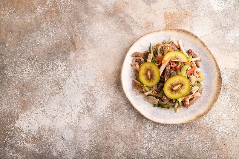 Meat salad with beef kiwi and vegetables on brown concrete background. top view, flat lay, copy space