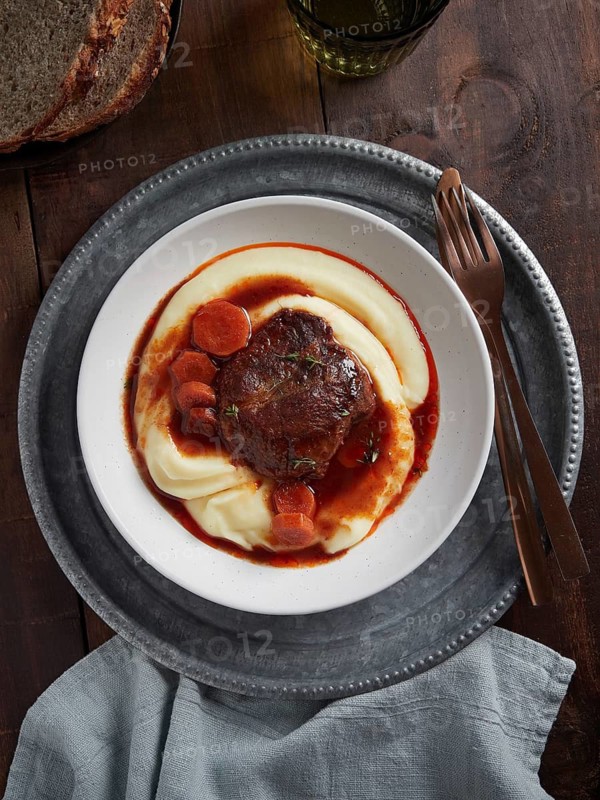 Braised pork cheeks with carrots and gravy over mashed potatoes. Spanish food. View from above, plate on wooden table