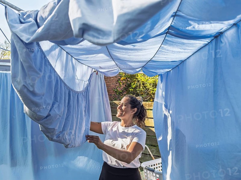 A cheerful woman attends to daily chores in an Australian backyard, hanging fresh laundry on a clothesline under the sun. A snapshot of everyday life and domesticity