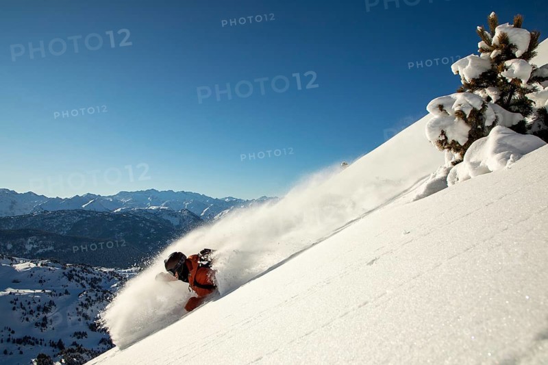 A skier in dynamic action, carving through fresh powder on a steep slope Crisp snow swirls vividly against the clear blue sky, capturing the thrill of freeride skiing