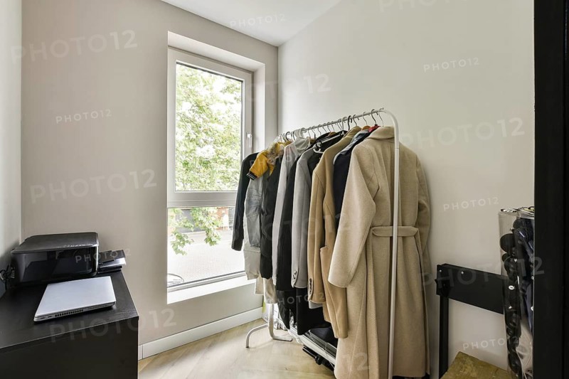 A clean, minimalist interior featuring a clothing rack laden with various garments next to a window, enhancing the space's light and openness