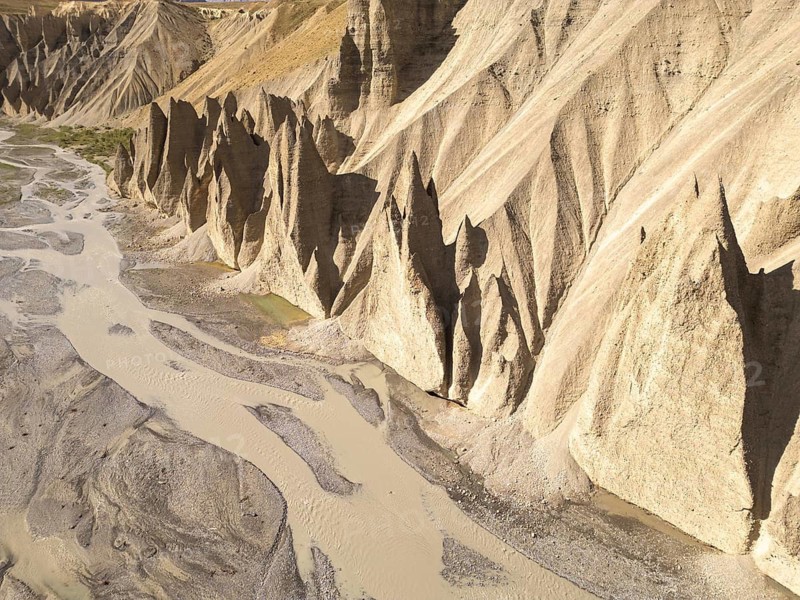 Rugged, steep cliffs rise dramatically from the ground, molded over time by natural erosion in Spiti Valley, India. A meandering river completes this striking scene