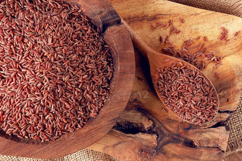 Natural, red rice, in a wooden bowl and spoon on a wooden surface in rustic style, top view