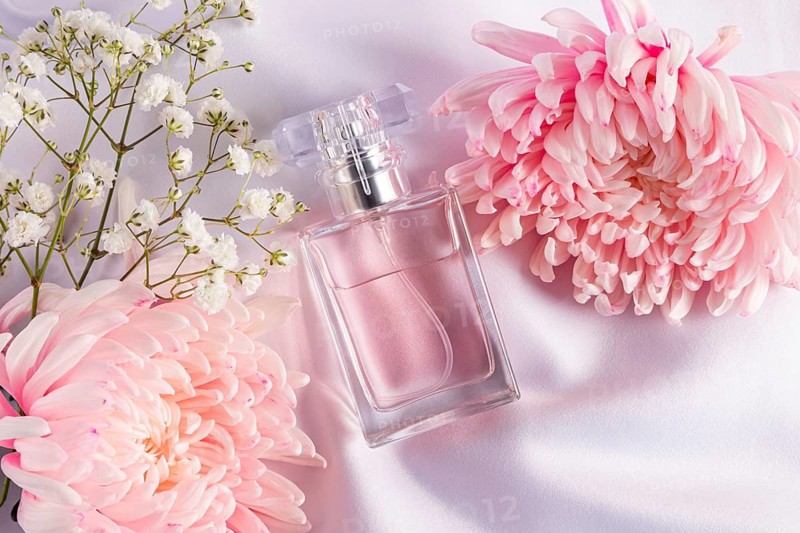 An elegant scene featuring a pink perfume bottle surrounded by delicate pink and white flowers on a soft background. The setting exudes a sense of luxury and femininity