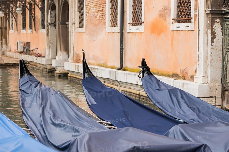 Covered gondolas float serenely beside a historic Venetian building, showcasing the unique beauty of Venice waterways and the graceful charm of its age old architecture