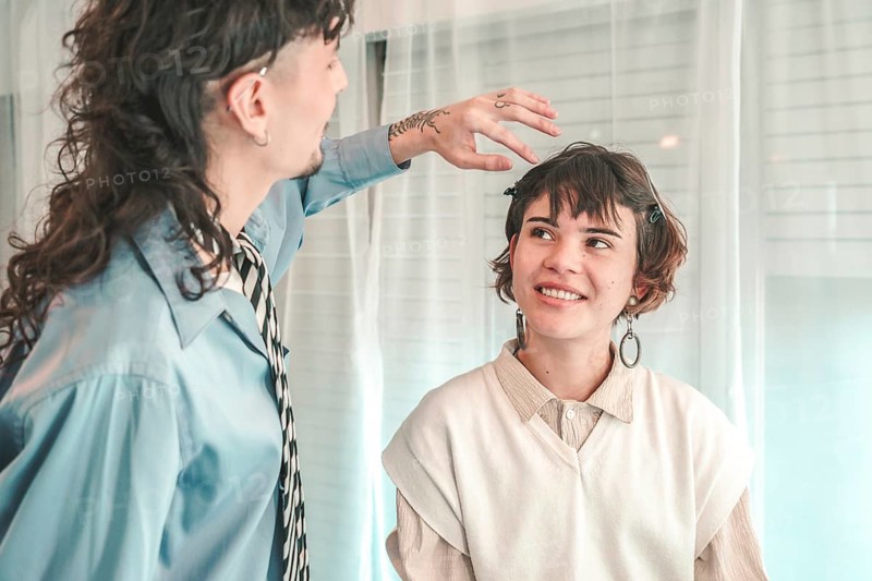 Hairdresser gently placing hand on client's head, preparing for a haircut in a bright and airy salon, showcasing a moment of connection and personalized service