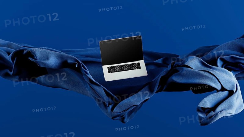A sleek laptop is placed atop smooth fabric, showcasing its lightweight design against a rich blue backdrop