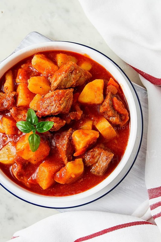Potatoes stewed with meat, in tomato sauce, with spices and herbs, no people, on a white table