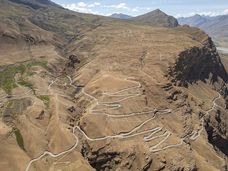 A stunning aerial view captures the winding roads of Spiti Valley, India, showcasing the rugged, mountainous terrain and contrasting green patches amid the arid landscape