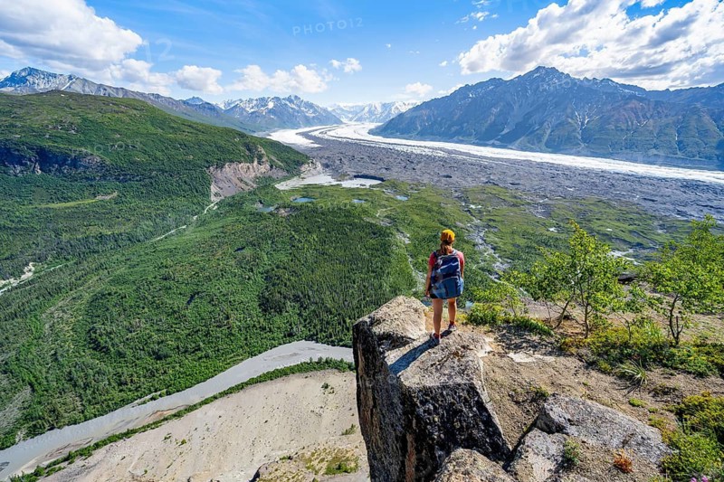 Young woman on a rocky outcrop enjoying the view, view of impressive mountain landscape with Matanuska glacier and glaciated mountain peaks, Lion's Head, Chugach Mountains, Alaska, USA