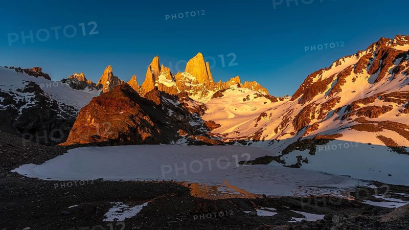 Fitz Roy massif with Cerro Fitz Roy and Cerro Poincenot in alpine glow at sunrise, frozen Laguna de los Tres, snow-covered rock peaks under clear skies, Los Glaciares National Park, Patagonia, Argentina