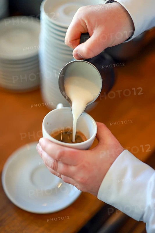 Germany - Barista prepares a coffee, here a cappuccino, hand pours milk foam from a pot into a cup with espresso coffee