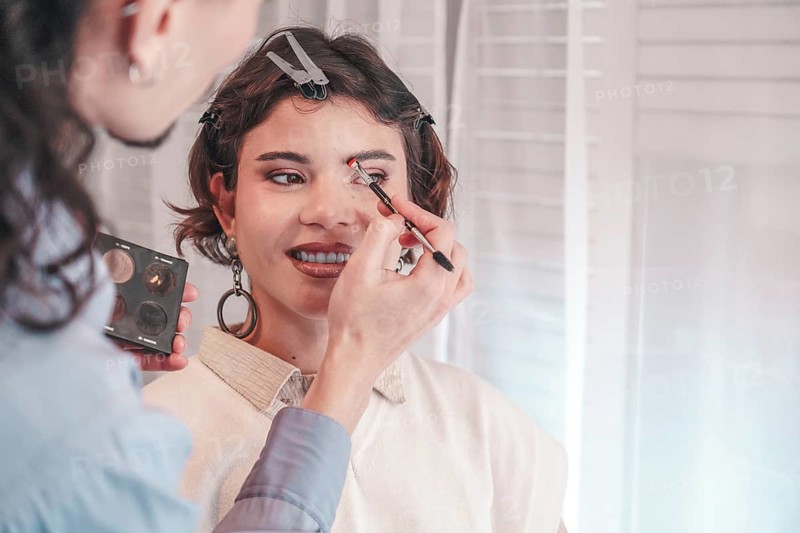 Professional makeup artist applying eyeshadow on a smiling model in a bright makeup studio, enhancing her beauty for a photoshoot or special event