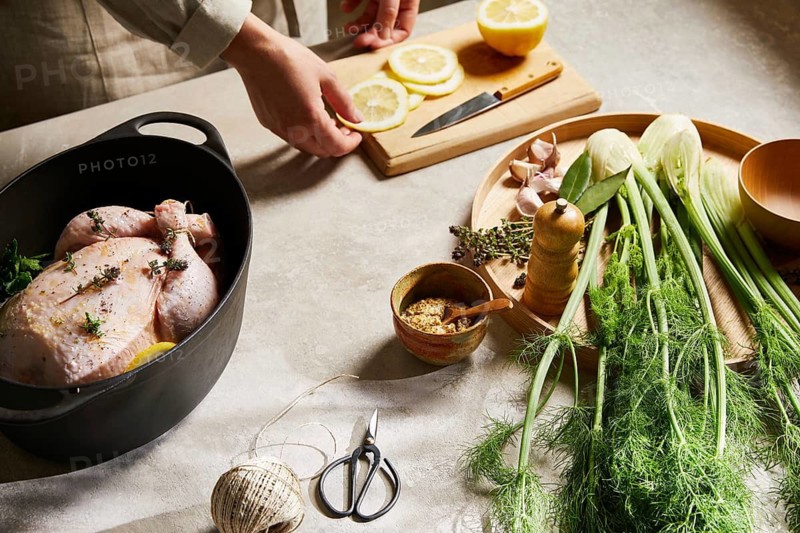 A butcher prepares a savory chicken dish with fresh ingredients, including lemon slices and fennel, showcasing culinary skills and attention to detail in a rustic kitchen setting