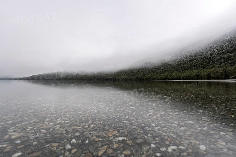 Clear lakeside with pebbles under water, fog-shrouded, wooded slopes, Tierra del Fuego National Park, Tierra del Fuego, Argentina