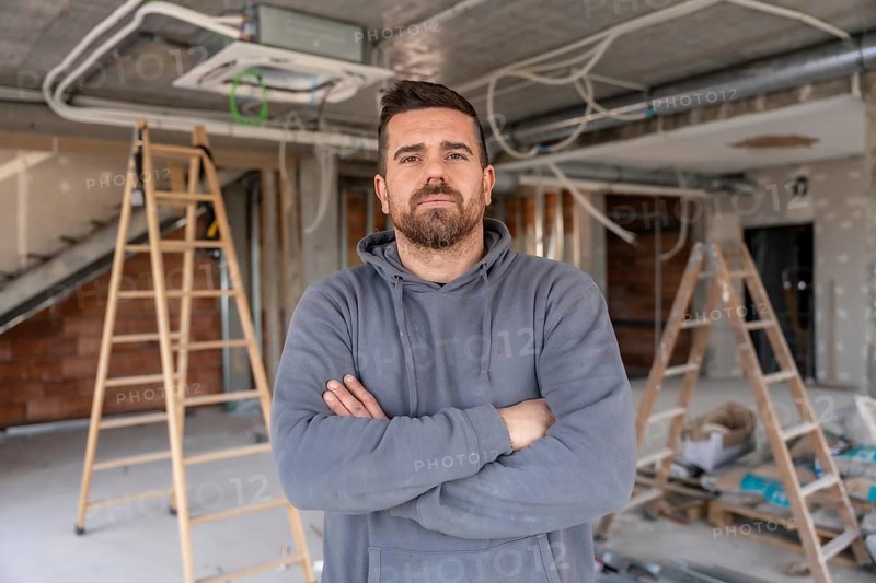 Air conditioning expert standing with crossed arms, looking at the camera, overseeing new hvac systems installation and renovation process in a building under construction