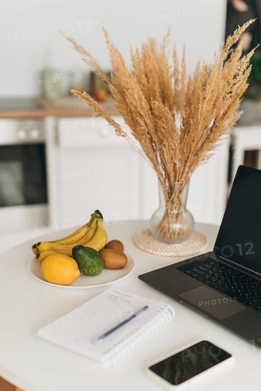 A clean workspace featuring a laptop, open notebook, and a plate of fresh fruits including bananas, avocado, and lemon, symbolizing nutrition and healthy living