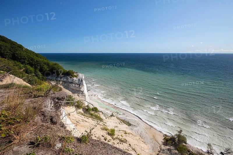 White chalk cliffs in August. People on the beach and by a small lagoon. Milky Baltic Sea under a blue sky. Møns Klint, Sjælland, Denmark