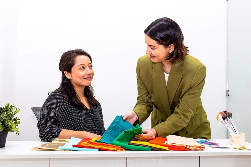 A professional image consultant assists a woman in selecting color swatches, aiming to enhance her personal style. The consultant offers personalized fashion advice in a modern office