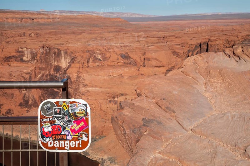 Page, Arizona - Although covered with unrelated stickers, a sign at the Horseshoe Bend overlook along the Colorado River still warns of danger. The overlook is about a thousand feet above the river